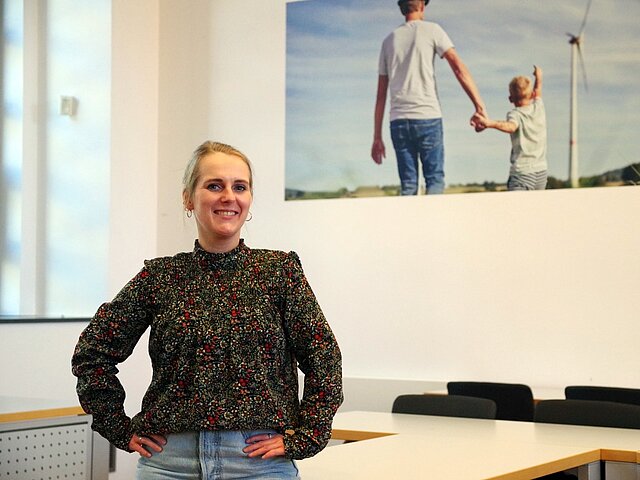 Ramona, Mitarbeiterin bei JUWI, lehnt an einem Schreibtisch und lächelt in die Kamera.